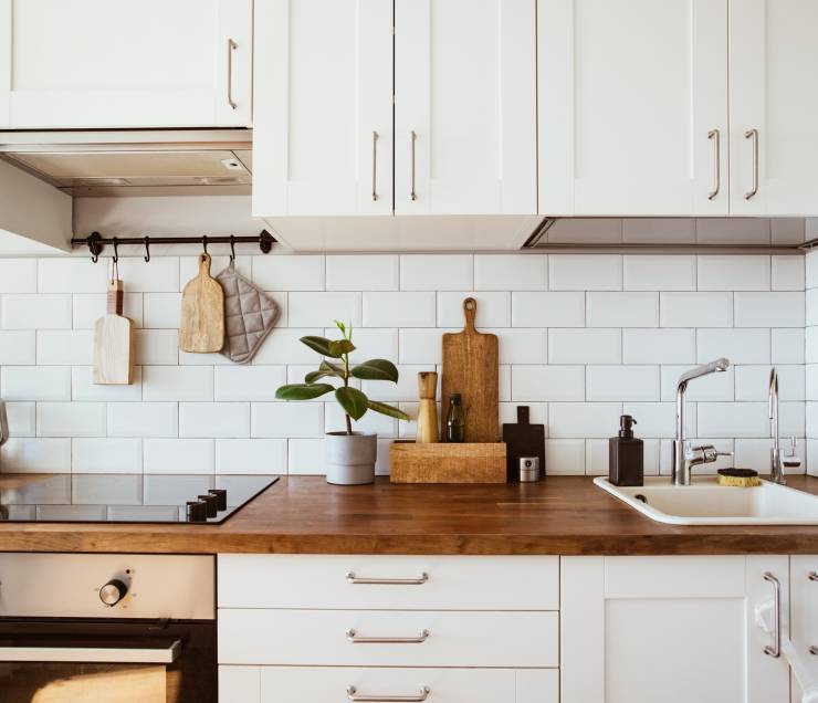 Kitchen brass utensils, chef accessories. Hanging kitchen with white tiles wall and wood tabletop.Green plant on kitchen background side view
