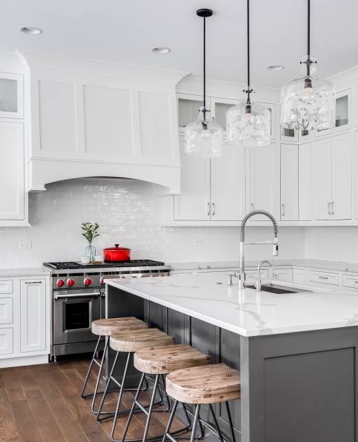 A large luxury kitchen with white granite countertops and cabinets, stainless steel appliances, hardwood floors, and glass pendant lights hanging above.